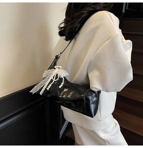 Detail of glossy black shoulder bag with lace bow and pearl chain on a model