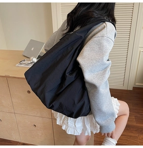 Side view of black nylon hobo tote bag worn by model in a cozy indoor lifestyle setting