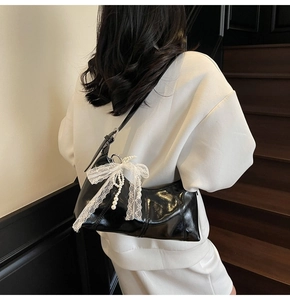 Detail of black glossy faux leather shoulder bag with white lace bow and pearls