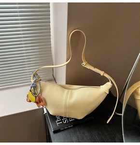 Detail of light yellow crescent bag with leather texture and cute elephant pendant decor