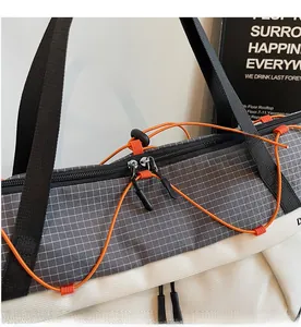 Detail of smooth double zipper and orange drawstring on a grey checkered sports bag