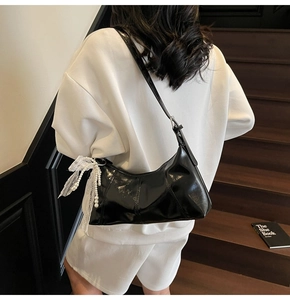 Detail of black patent leather shoulder bag with white lace bow and pearl charm pendant