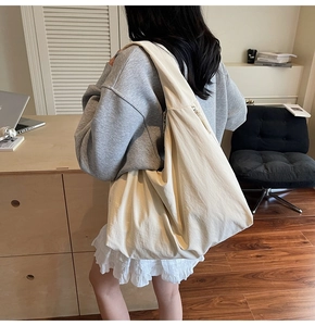 Close-up of a minimalist beige tote bag worn on shoulder in a cozy indoor setting