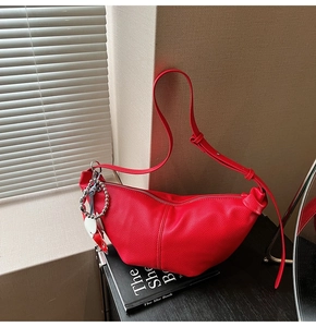 Red pebbled leather crescent crossbody bag shown with a chic book on a textured background
