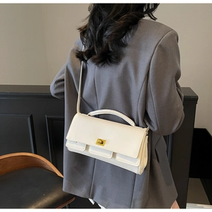 Detail of white leather handbag with golden twist lock on a grey suit-wearing model
