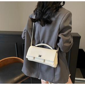 Close-up of a cream leather baguette bag with silver metal buckle on a gray blazer