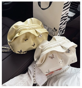 Detail of cream pleated bucket bag featuring silver butterfly buckle and chain strap