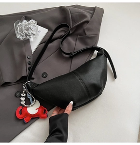 Detail of black lychee leather crescent bag with elephant charm on grey suit background