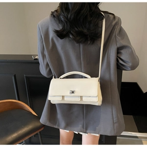 Model wearing a cream white leather square handbag with silver metal lock on a grey suit