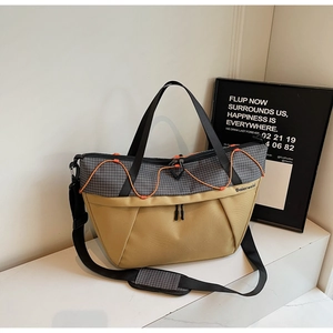 Detail of khaki and gray canvas duffel bag with bright orange drawstring on a white podium