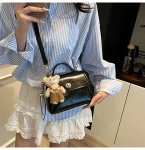Detail of black glossy handbag with gold circular twist lock and cute teddy bear charm