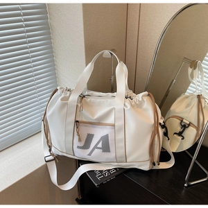 Detailansicht der beigefarbenen Reisetasche mit JA-Logo auf schwarzem Holzschrank