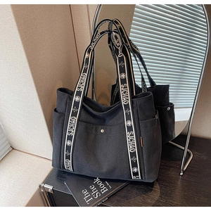 Detail of large black canvas tote with patterned shoulder strap and metal snap button pocket
