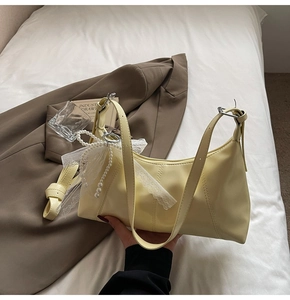 Detail of creamy yellow shoulder bag featuring vertical stitching and pearl bow charm