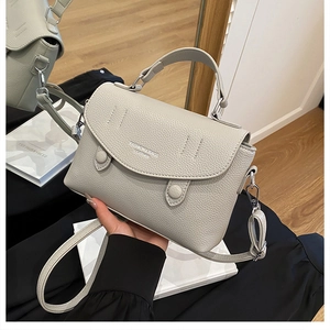 Detail of gray litchi texture leather bag with fashion logo and adjustable strap