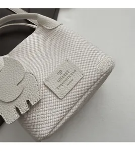 Close-up of white woven bucket bag featuring lychee grain leather charms and fine texture