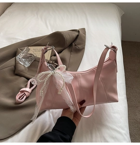 Detail of pink shoulder bag featuring decorative pearl strings and a white lace bow accent