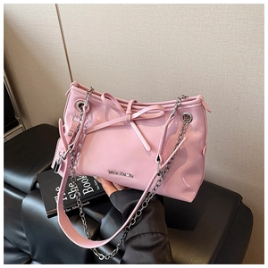 Close-up of pink glossy shoulder bag featuring a metal bow, chain strap and letter logo