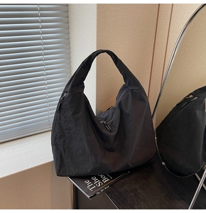 Detail of black nylon tote bag showing wrinkled texture and metal zipper pockets