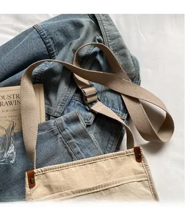 Dettaglio tracolla regolabile in tela beige con fibbia in pelle marrone e rivetti