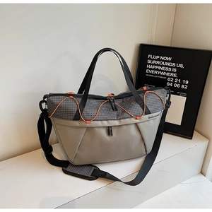 Detail of grey crossbody bag with orange bungee cords and plaid shoulder pad