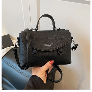 Close-up of black litchi pattern leather handbag featuring elegant metal strap hardware