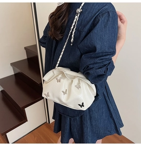Close-up of white pleated bucket bag with butterfly charms and chain strap on model