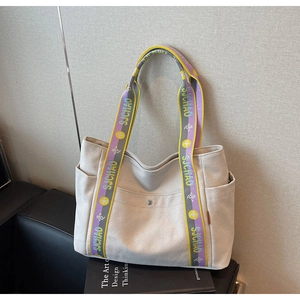 Detail of canvas tote bag featuring wide yellow and purple logo straps and side pockets