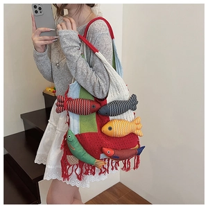 Detail view of a colorful knitted tote bag featuring 3D fish dolls and red fringe tassels