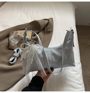 Detail of light blue shoulder bag featuring white lace pearl bow and adjustable metal buckle