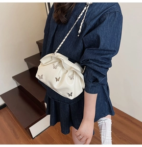 White ruched cloud bucket bag with silver butterfly charms worn with a denim dress