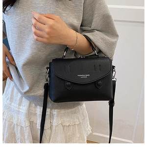 Close-up of black lychee grain leather crossbody bag with top handle and fashion text