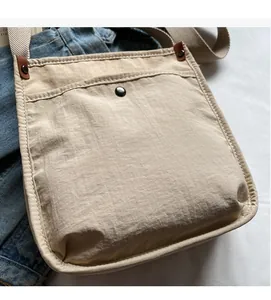 Dettaglio borsa a tracolla in tela beige chiaro con chiusura in pelle e bottone a pressione