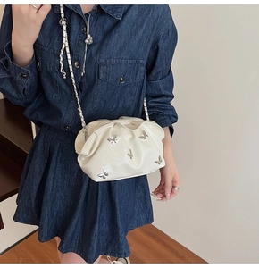 Detail of white pleated bucket bag with silver butterfly charms and chain strap