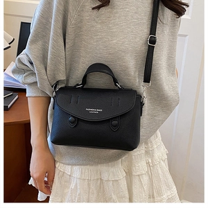 Detail of black litchi grain leather crossbody bag showing fashion text and silver buckle