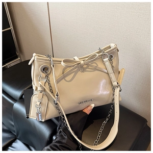 Close-up of beige leather handbag with chain strap, bow detail and silver lock charm