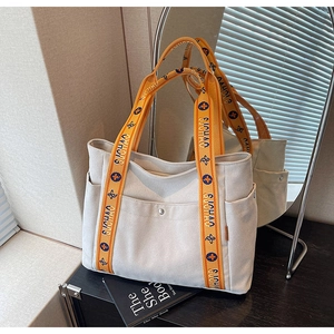 Close-up of cream canvas tote bag with orange graphic straps and metal button pocket