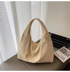 Detail of minimalist beige hobo bag with zip pockets and textured fabric on a soft bench