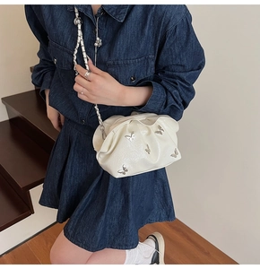 Close-up of white bucket bag with silver butterfly charms and metal chain strap
