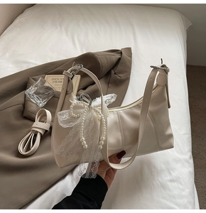 Detailed view of beige leather shoulder bag with decorative pearl lace bow charm and strap