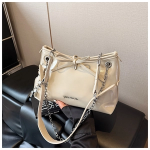 Close-up of beige glossy handbag featuring a large bow detail and gold metal chain strap