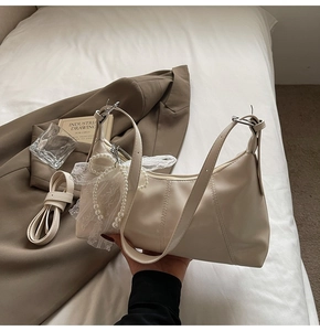 Detail of cream white dumpling bag featuring pearl string and delicate lace charm