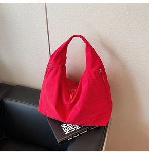 Detail of red large capacity tote bag with nylon texture and zipper pockets on a sofa