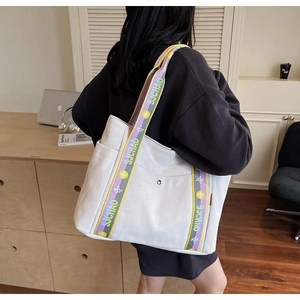 Detail of canvas tote bag with purple and yellow woven strap in casual indoor setting