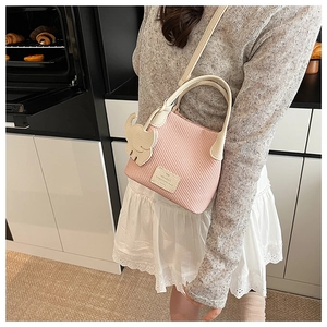 Pink woven mini handbag with white elephant charm and thin crossbody strap on model