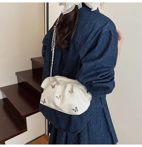 White pleated bucket bag with silver butterfly charms worn by a model on a shoulder