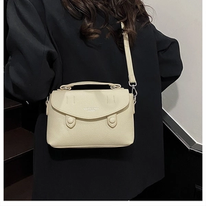 Detail of light beige pebbled leather texture and silver hardware on a crossbody bag