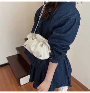 White pleated cloud bucket bag featuring silver butterfly charms and chain strap