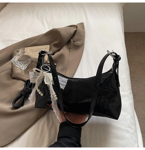Close-up of black leather underarm bag with elegant white lace bow and pearl charms