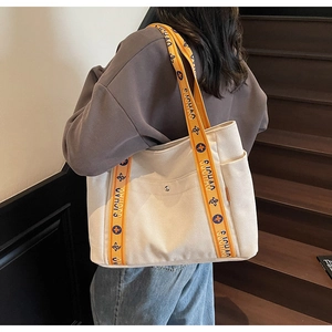 Detail of canvas tote bag featuring orange patterned strap and metal button front pocket